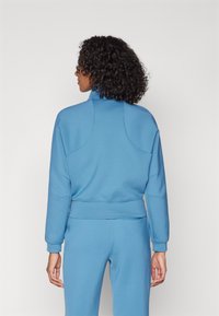 Blauer Pullover mit hohem Kragen, weichem Stoff und geripptem Saum. Mit überschnittenen Schulternähten und engen Bündchen, kombiniert mit passenden Hosen.