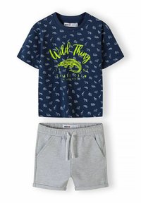 Camisa de manga corta azul marino con estampados de animales claros y texto en verde neón que dice "Wild Thing", combinada con pantalones cortos grises claros con cintura elástica y cordón.