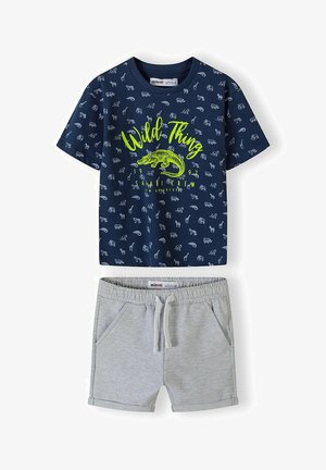 Mørkeblå kortærmet skjorte med lyse dyreprint og neongrøn tekst "Wild Thing", parret med lyse grå shorts med elastisk liv og snore.