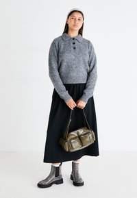 Pull en tricot gris avec un col et des boutons, jupe noire, bottines argentées brillantes, et un sac à main vert olive avec des poches.