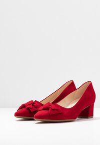 Chaussures à talons hauts en daim rouge avec un bout arrondi et un nœud décoratif à l'avant. Talon carré et doublure intérieure lisse.