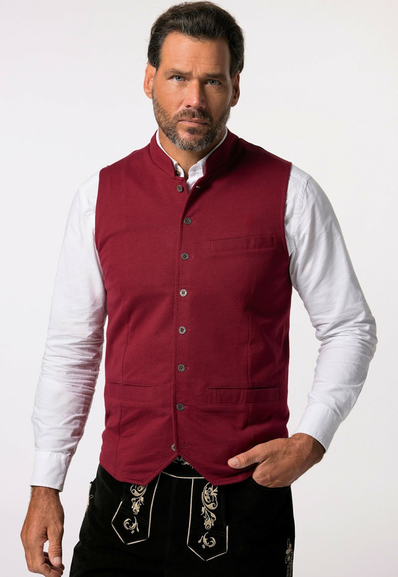 Chaleco de algodón burdeos con cuello mao, botones frontales y dos bolsillos. Llevado sobre una camisa blanca, combinado con pantalones negros bordados.