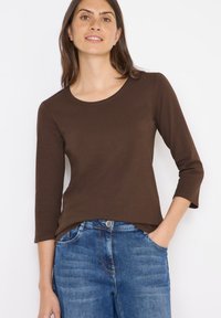 Maglia marrone a maniche lunghe con scollatura rotonda, realizzata in un tessuto morbido. Abbinata a jeans in denim blu con una texture sbiadita e tasche.