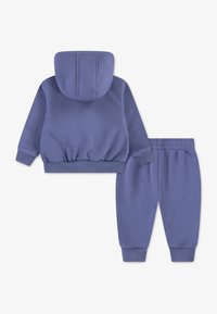 Dvojdielny outfit z jemnej fialovej tkaniny, zahŕňajúci mikinu s kapucňou a rebrovaným lemom a zodpovedajúce vypasované nohavice s elastickým pásom.