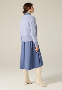 Maglione azzurro chiaro a maglia con un motivo testurizzato, abbinato a un vestito blu fluido e stivali al ginocchio beige.