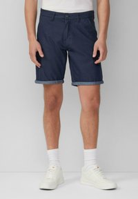 Marineblaue Shorts aus Denim, mit einem Knopfverschluss und umgeschlagenen Säumen, kombiniert mit weißen Sneakers und gerippten Knöchel-Socken.