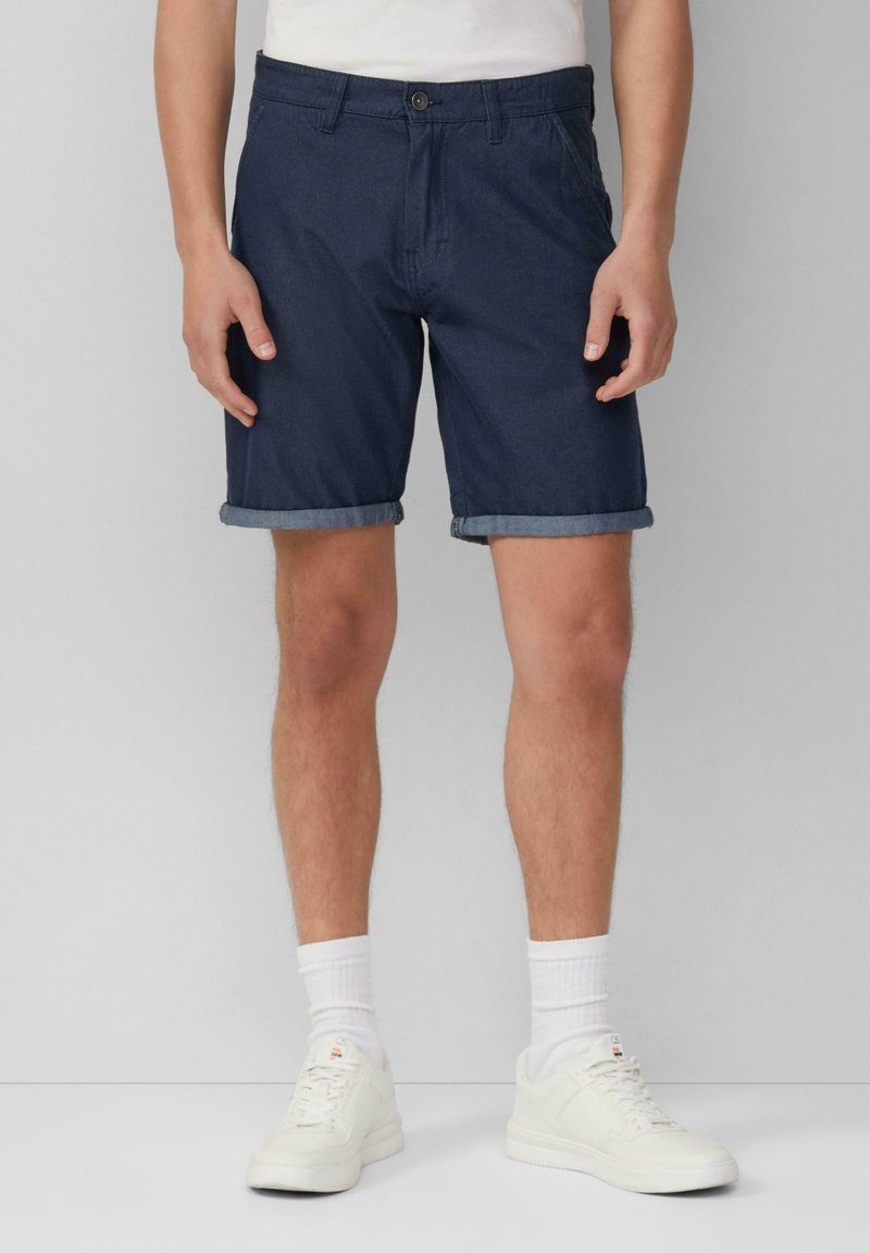 Marineblaue Shorts aus Denim, mit einem Knopfverschluss und umgeschlagenen Säumen, kombiniert mit weißen Sneakers und gerippten Knöchel-Socken.