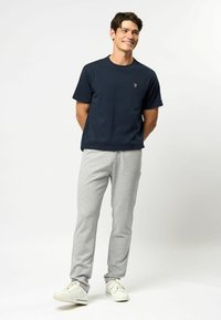 Navy cotton t-shirt with crew neck and small logo, paired with light gray sweatpants. Casual white sneakers complete the outfit.