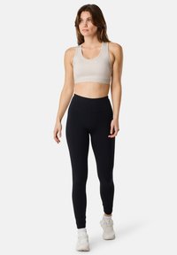 Soutien-gorge de sport gris clair avec une bande élastique texturée, associé à un legging noir taille haute. Les deux sont conçus pour être portés lors d'activités physiques.