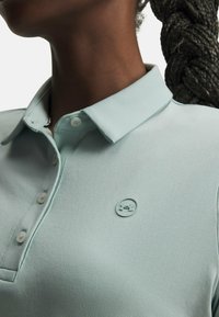 Ανοιχτό τιρκουάζ πόλο πουκάμισο από απαλό ύφασμα, με κλασικό γιακά και τρία κουμπιά, με διακριτικό λογότυπο στην αριστερή πλευρά.