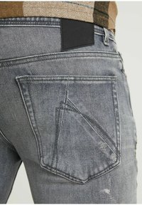 Grå denimjeans med en distinkt design, en texturerad yta och unika ficksydda detaljer. Svart läderpatch vid midjan.