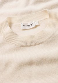 Helle beigefarbene Strickjacke mit einem gerippten Rundhalsausschnitt. Weiche Textur, normale Passform und ein Etikett mit der Aufschrift "hessnatur" Größe S.