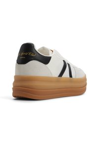 Sneaker bianca con accenti neri e una suola in gomma spessa. Presenta una tomaia testurizzata, un sistema di allacciatura e un logo in rilievo sul tallone.