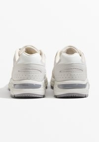 Fehér hálós és bőr sportcipők párnázott gallérral, szürke részlettel a talpon és perforált részletekkel az oldalakon.