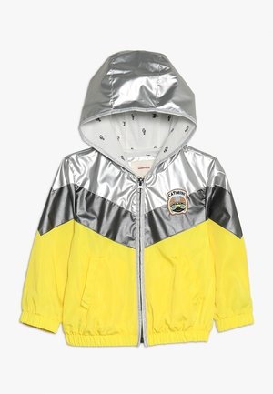 Veste à capuche pour enfants avec des blocs de couleur argent, gris et jaune, fermeture éclair sur le devant, poches latérales et un écusson logo Catimini sur la poitrine.