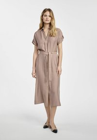 Jasnobrązowa sukienka do kolan z krótkimi, podwiniętymi rękawami, z przodu zapinana na guziki i związywana w pasie. Gładka faktura, casualowy styl.