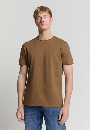 Braunes kurzärmliges T-Shirt aus weicher Baumwolle, mit Rundhalsausschnitt und kleinem Logo auf der Brust; kombiniert mit blauen Jeans.