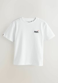 Camiseta de algodón blanca con mangas cortas, escote redondo y un pequeño logo de Superdry en el lado izquierdo del pecho. Textura suave, diseño sencillo.