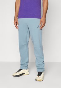 Lyseblå joggebukser med et tapered design, fremstillet af blødt stof, med sort logo broderi og sidelommer. Båret med hvide sneakers.
