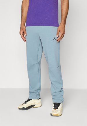 Light blue jogger pants with a tapered design, made of soft fabric, featuring black logo embroidery and side pockets. Worn with white sneakers.