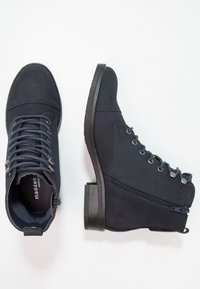 Stivaletti alla caviglia blu navy con finitura testurizzata, stringati frontalmente, con zip laterale e tacco basso a blocco. Presentano occhielli in argento e dettagli di cucitura.