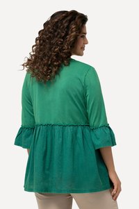 Grünes Baumwolloberteil mit Dreiviertel-Bellärmeln, ausgestattet mit einem rüschengeschmückten Saum und glatter Textur. Einfaches, lockeres Schnittdesign.