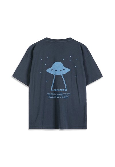 T-shirt bleu foncé avec un design pixellisé d'un OVNI bleu clair et le texte "ALL ABOUT MONSTERS" au dos.