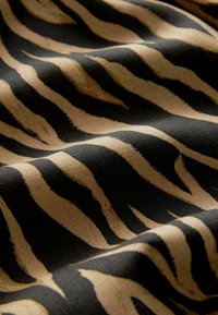 Material cu un model de dungi de zebre, cu dungi negre intense pe un fundal beige, evidențiind o aparență texturată, țesută.