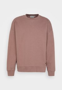 Sudadera rosa empolvado con escote redondo, textura de canalé, mangas raglán y bajo acanalado. Sutil acento de logo en el lado inferior.