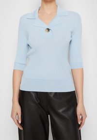 Jasnoniebieski sweter z prążkowanego materiału, z kołnierzykiem i pojedynczym ozdobnym guzikiem. Posiada rękawy do łokcia i dopasowany fason.