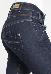Mörkblå denimjeans med en åtsittande design, flera fickor, kontrasterande sömmar och en läderetikett på midjebandet.