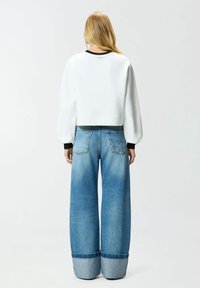 Felpa bianca corta con scollo nero, abbinata a jeans denim blu a gamba larga con risvolto azzurro chiaro e texture sfumata.