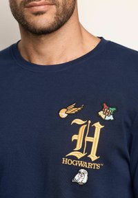 Camiseta de algodón azul marino con logo de Hogwarts bordado, con diseños de quaffle, emblema de la casa y búho. Cuello redondo, corte estándar.