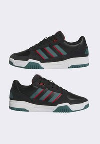 Zapatillas deportivas negras con una combinación de cuero y ante, que presentan rayas en teal y rojo, suela blanca y detalles texturizados en el talón.