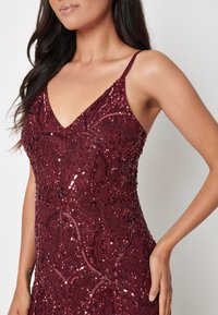 Bordeaux-mekko, jossa on V-pääntie, ja jota korostavat paljetit ja helmikoristelu kukkakuoseilla. Ohut olkaimeton malli ja tiukka siluetti. Pehmeä rakenne.