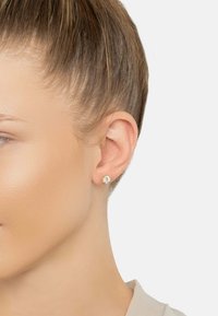 Gold-tone stud earring featuring a clear, round gemstone in a simple bezel setting, showcasing a smooth, polished finish.