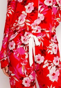 Rode bloemen pyjama set met grote roze en witte bloemen, een knoopsluiting aan de bovenkant en broek met een trekkoord en een witte strik. Soepele stoftextuur.