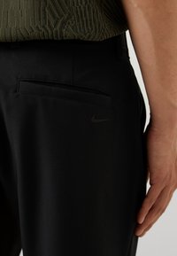 Sorte bukser laget av teksturert stoff, med en baklomme og en subtil svart Nike-logo, med en glatt overflate og en skreddersydd passform.