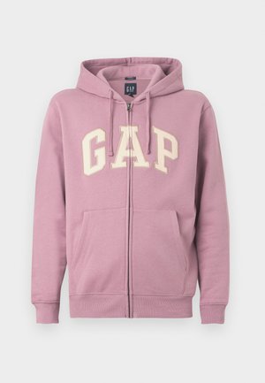 Vaaleanpunainen vetoketjullinen huppari, jossa on nyörit ja suuri vaalean kerma"GAP" -logo edessä. Hupparissa on kaksi etutaskua ja resorit hihansuissa.