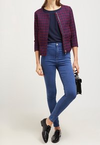 Czerwono-granatowa kurtka w szewrony o skróconym kroju z rękawami 3/4, zestawiona z dopasowanymi niebieskimi dżinsami i czarnymi lakierowanymi loafersami.