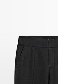Pantalon en lin noir avec une large ceinture et des poches latérales, présentant une texture lisse et un design minimaliste.