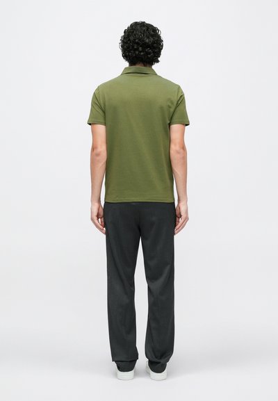 Olivzaļš polo krekls ar ribotu apkakli, kombinēts ar tumši pelēkiem biksēm un baltām sporta kurpēm, redzams no aizmugures.