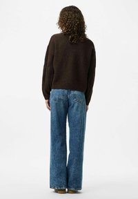Brązowy sweter dzianinowy, w oversize'owym kroju, z prążkowanym dołem, połączony z niebieskimi dżinsami w stylu dzwonów o wysokim stanie. Gładka faktura i swobodny fason.