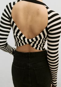 Haut à manches longues rayé noir et blanc avec un dos découpé, texture côtelée, associé à un jean en denim noir taille haute avec des poches arrière.