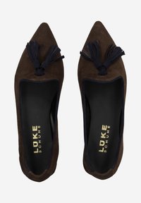 Ballerines pointues en daim marron avec des accents bleu marine, ornées de pompons à l'avant et présentant un intérieur lisse ; logo doré sur la semelle intérieure.