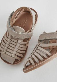 Beige lädersandaler med ett korsat mönster, öppen tå, justerbar rem och kontrasterande sömmar på en platt sula.