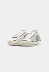 Gray canvas sneakers feature a low-cut design, round toe, and a textured sole with a white rubber rand and subtle star logo on the side.