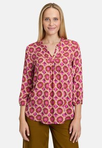 Blusa rosa con design a motivi geometrici in tonalità di rosa, arancione e bianco. Presenta un scollo a V e maniche a tre quarti.
