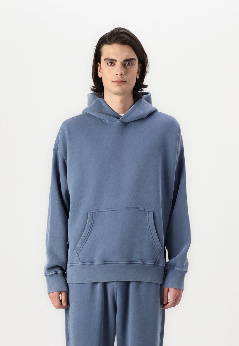 Hoodie bleu en mélange de coton, avec une poche avant, coupe oversize et capuche réglable avec cordon. Texture douce et poignets côtelés.