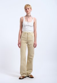 Beige džíny s vysokým pasem vyrobené z denimu, s rovnou nohavicovou siluetou a jemnými detaily šití. Nošeny s bílým topem na ramínka.
